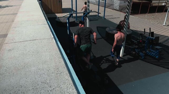 Anonymous male gymnast executing intense bodyweight exercise routine at urban outdoor street park. High angle shot of guys training triceps on parallel bars under bright midday summer sunlight