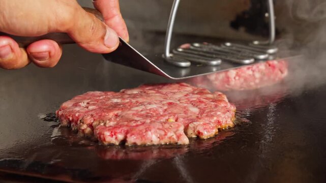 Pressing raw meat patty ball onto hot grill for smash burger cooking