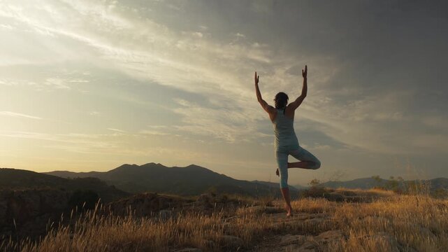 Woman finding serenity in yoga tree pose at golden hour sunset, embodying balance and inner peace in a vast open landscape, promoting mindfulness and outdoor wellness.