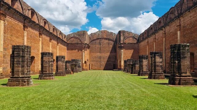 Sunny view of the UNESCO-listed Jesuit Mission of Jes&uacute;s de Tavarang&uuml;&eacute; in Paraguay, featuring monumental brick walls and towering columns rising above vibrant green grass