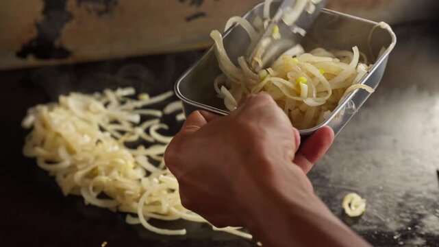 A person scooping hot steamy cooked onions into a bowl after cooking in a flat griddle