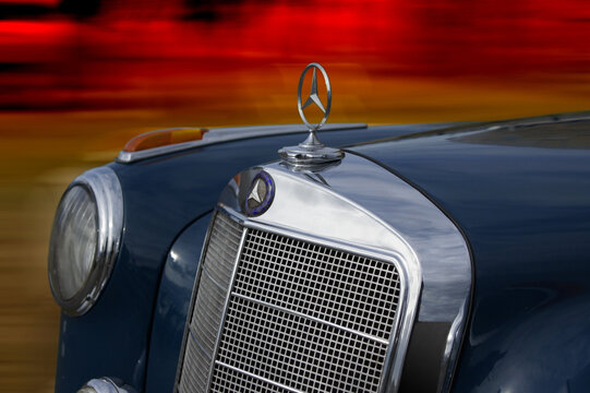 Old Mercedes - Benz chrome plated sign and grill on front of classic 219 model car. Blurred and coloured background.