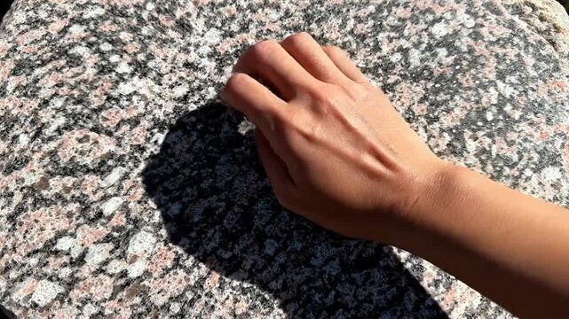 A hand pressing flat against a rough granite rock surface from a top-down perspective, emphasizing texture and natural material.
