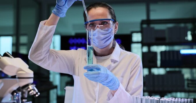 Woman scientist raises pipette above glass tube in lab. Gloved hand releases blue reagent measuring sample during careful testing work slow motion