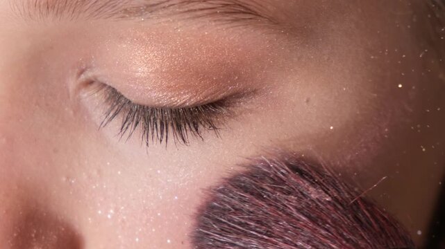 Close-up of a makeup brush applying highlighter or shimmer powder to a woman's cheek. Beauty routine, professional makeup application, glowing skin and cosmetic skincare concept