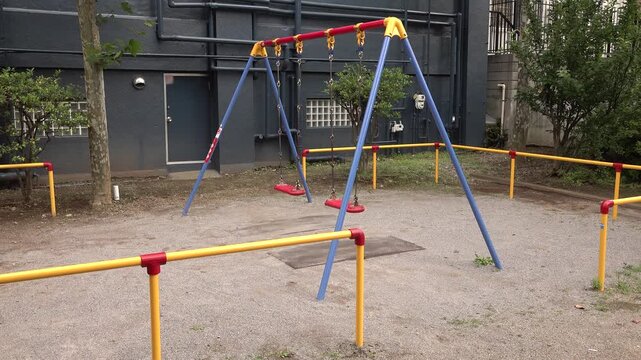 Empty red swings behind a yellow fence in a small Japanese park