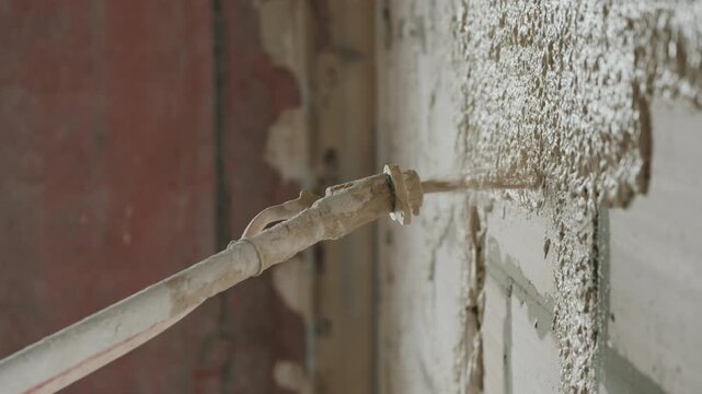 Spraying plaster mortar onto masonry wall with plastering machine