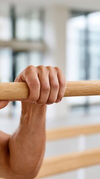 A hand grips a rehabilitation parallel bar firmly, showing focus on physical therapy. The setting is a training area with soft light