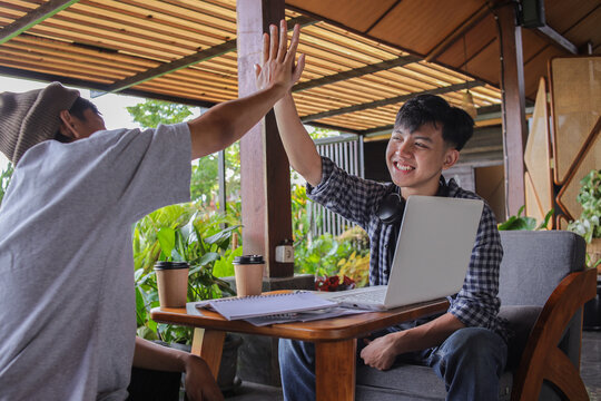 Two Asian Men Sit At Wooden Table In An Outdoor Cafe
