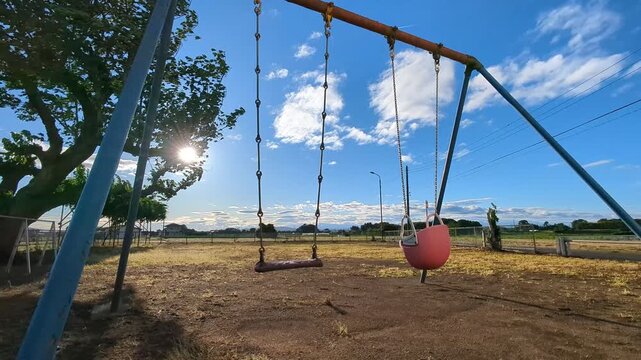 4K slow‑motion shot of an empty swing swaying in the wind at a rural park with backlit sunlight through tree branches