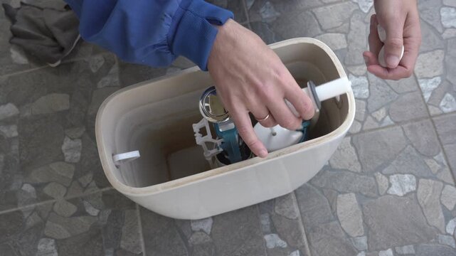 Close-up of the installation of the internal fittings of a ceramic toilet tank, Replacing the toilet flush mechanism, Plumber installs the flush valve inside the ceramic toilet tank.