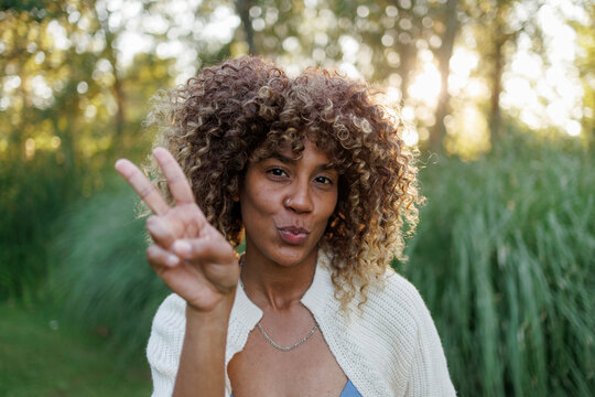 Young woman with curly hair showing a peace sign and making a kissy face