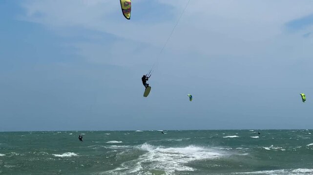 A dynamic action video showcasing a skilled kitesurfer riding choppy sea waves, catching the wind, and executing an impressive, high-altitude jump against a partly cloudy sky.