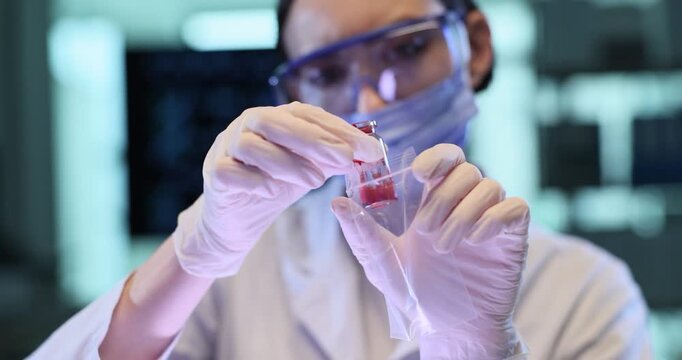 Female technician puts vial with red liquid into plastic bag in lab. Forensic professional prepares crime evidence for storage in police laboratory