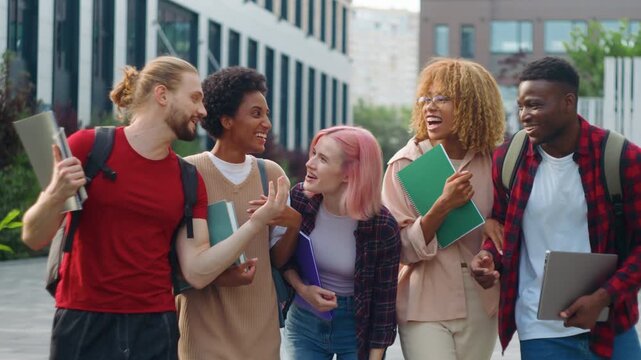 Five happy multiracial students talking laughing humorous discussing ridiculous news joke cuddling walking in city multiethnic friends talk laugh joyous cuddle walk near university college outdoor