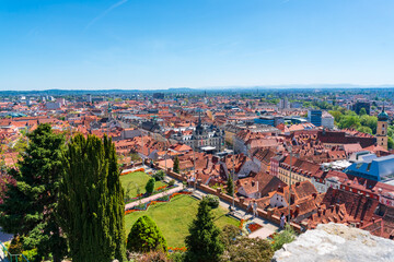 Naklejka premium Wide panoramic cityscape of Graz viewed from Schlossberg Hill with landscaped gardens, historic center, and distant horizons under a clear blue sky