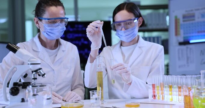 Female chemist takes sample of oil from beaker as colleague controls test in lab. Scientists study yellow liquid properties in glassware at workplace