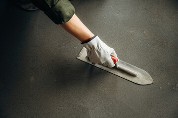 Obraz premium Hand of a construction worker wearing a glove using a trowel to smooth wet concrete surface on a floor during renovation or construction project