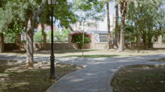 Blurred park path with soft bokeh and trees, stone paving and lamppost out of focus; background backplate copyspace calm.