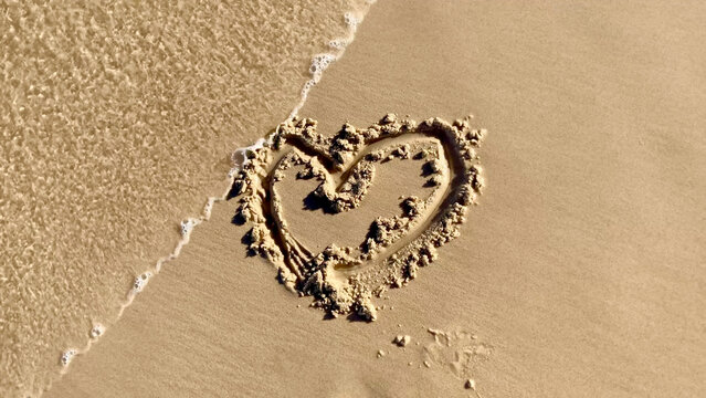 Heart shape drawn in wet sand on beach with water approaching