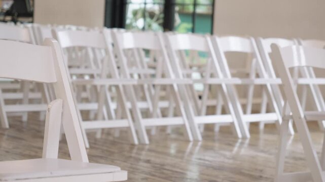 Rows of white folding chairs are neatly arranged in a bright venue, ready for a wedding ceremony. Ideal for event planning visuals or wedding promotional content.