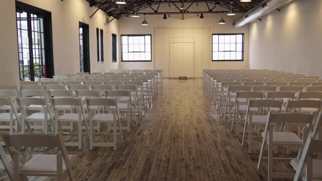 Rows of white folding chairs are neatly arranged in a bright room with wooden flooring. Ideal for event planning or venue showcases.