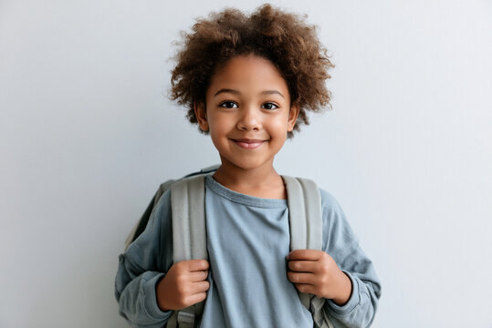 First grade student holding backpack and smiling, clean light wall background, copy space