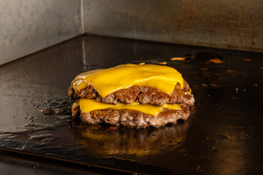 Close up of two juicy beef burger patties stacked with melted cheddar cheese on a hot flat top griddle