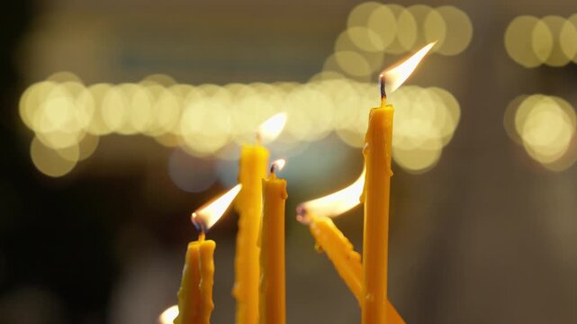 A POV shot looks at five candles burning and melting over time, against a beautiful bokeh backdrop of lights at a candlelit procession.