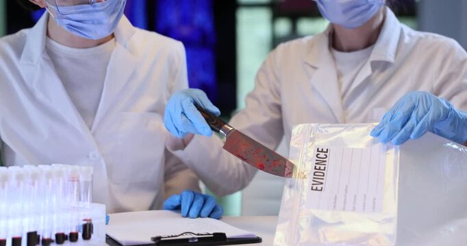 Women assistants take bloody knife out of plastic bag in lab. Female criminal professionals in masks study murder weapon in police laboratory