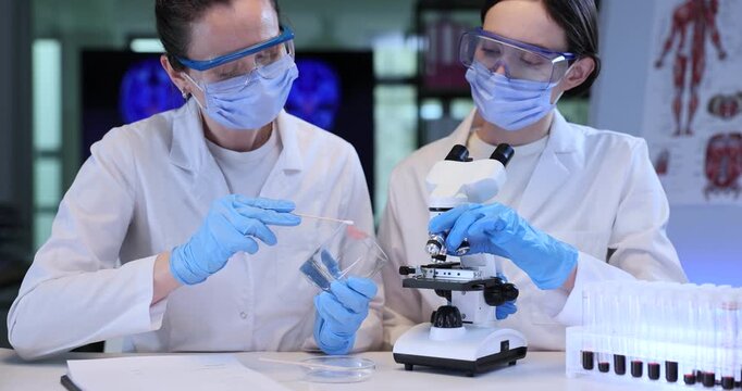 Forensic scientist puts specimen from glass onto colleague microscope slide in lab. Female criminalists analyze evidence from crime scene in workplace