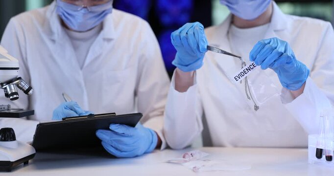 Police expert takes out silver necklace from package and assistant fills report in lab. Forensic professionals study jewelry evidence in laboratory