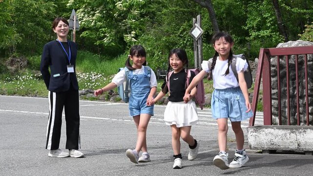 学校の校門で先生に見守られ手をつないで登校する女子小学生たち