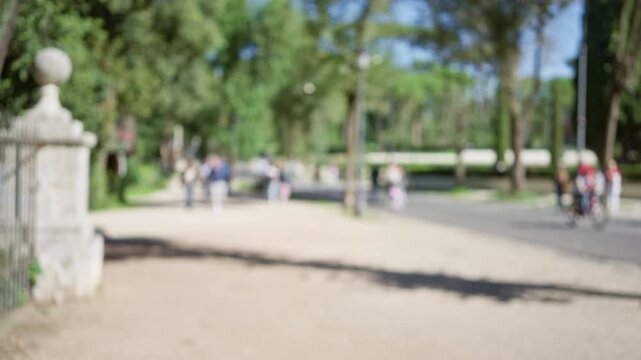 Blurry silhouettes of people strolling through villa borghese gardens in rome with trees and pathway in soft focus creating a serene outdoor ambiance.