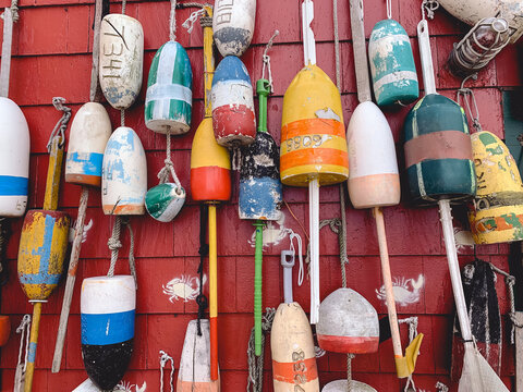 Collection of colorful, weathered lobster buoys hanging on a bright red fishing shack wall. Coastal maritime decor and New England fishing heritage captured in a detailed close-up.