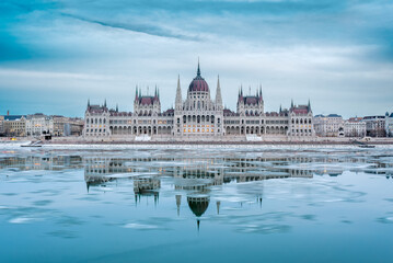 Obraz premium Hungarian Parliament Building symmetrical reflection in the frozen Danube River, winter twilight in Budapest, Hungary