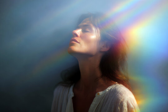 Woman inhaling light with soft rainbow rays across her face for spiritual healing background and wellness design