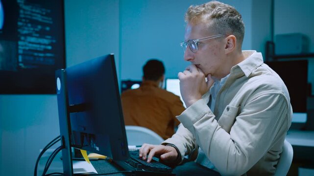 Young male software developer typing and reviewing code while designing website and AI system on computer in tech office workspace