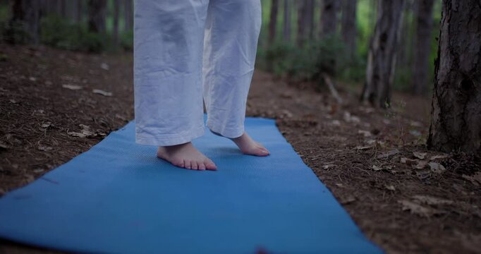 Barefoot practice of gentle foot exercises and balancing on a blue yoga mat, performed in the serene and natural setting of a forest, promoting wellness and mindfulness.