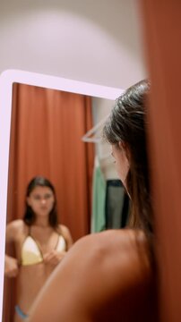 Reflective woman evaluates fit while dressing in boutique fitting room