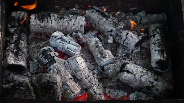 Birch firewood has completely burned down, turning into smoldering coals covered with white ash. The hot embers inside the barbecue grill are perfectly ready for cooking shashlik or BBQ