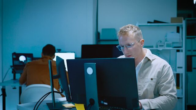 Young male software developer typing and reviewing code while designing website and AI system on computer in tech office workspace