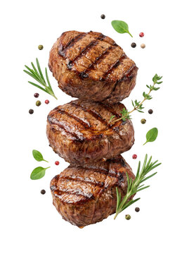 Three grilled beef steaks stacked vertically with fresh rosemary, thyme, and peppercorns isolated on transparent background