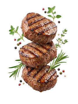 Three grilled beef steaks stacked vertically with fresh herbs and peppercorns isolated on transparent background