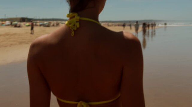 Woman standing on a sunny beach with calm sea and distant shoreline