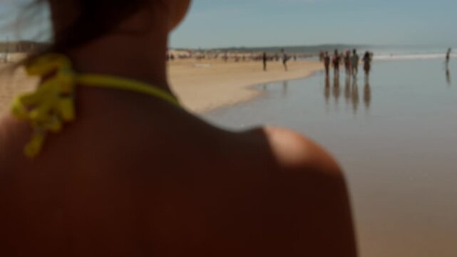 Woman standing on a sunny beach with blurred shoreline and distant people