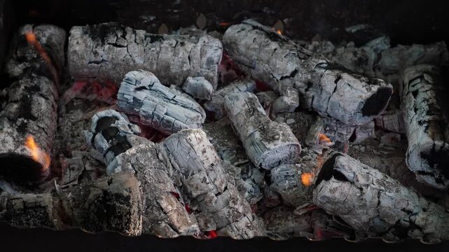 Close-up of smoldering firewood in a barbecue grill with light smoke and flames. Glowing charcoal covered with gray ash ready for BBQ.