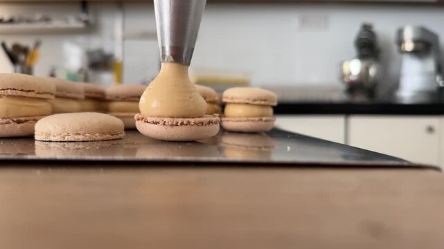 Detailed macro shot of salted caramel ganache piped onto French macaron shells during confectionery production