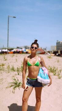 Woman standing on a sandy beach with phone and towel