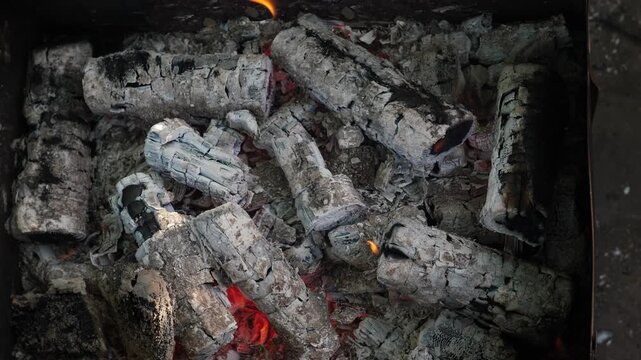 Hot coals and logs in the barbecue grill, top view. Glowing heat under a layer of gray ash and small flames for cooking